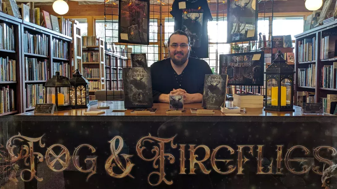 Author T.H. Lehnen tabling at Chaparral Books PDX on April 4, 20224, with posters, bookmarks, buttons, and t-shirts, and firefly lanterns lighting the table.